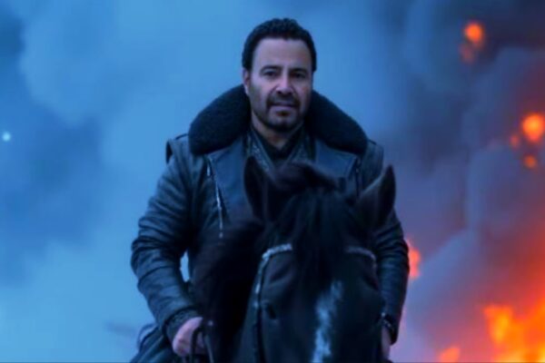 صورة للفنان عاصي الحلاني يقف ببسالة فوق حصان وسط خلفية من النيران والدخان، مرتديًا معطفًا داكنًا، يعكس قوة ودراما الأغنية "أشتكي لله" بتقنية الذكاء الاصطناعي.