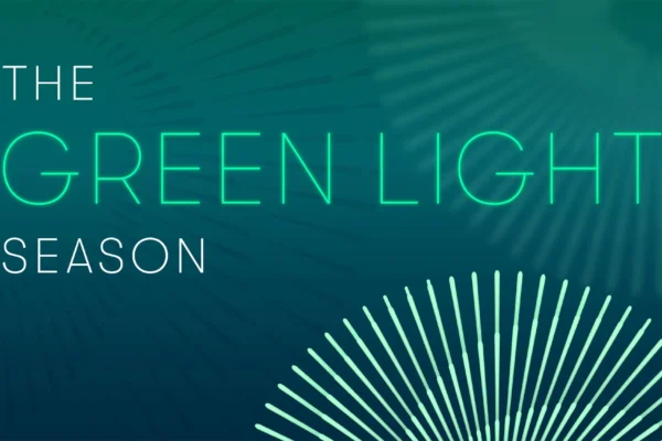 صورة نابضة بالحياة تحتوي على نص "موسم الضوء الأخضر" مكتوبًا بحروف نيون خضراء متوهجة على خلفية تيل أسود مع تصميم شعاعي يشبه الشمس، يرمز إلى الاستدامة والمبادرات الصديقة للبيئة في صناعة الترفيه.