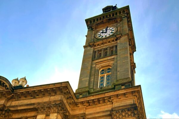 A historic clock tower of Birmingham Museum & Art Gallery against a clear blue sky, showcasing its architectural details and timepiece.