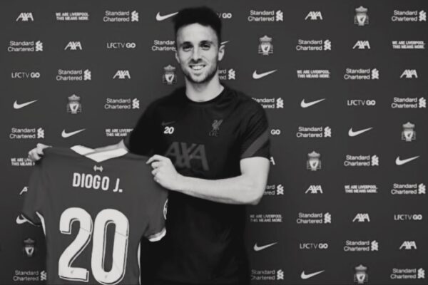 صورة للاعب ديوغو يوتا Diogo Jota وهو يحمل قميص ليفربول رقم 20 أمام خلفية النادي. Caption: ديوغو يوتا Diogo Jota في لحظة فخر مع