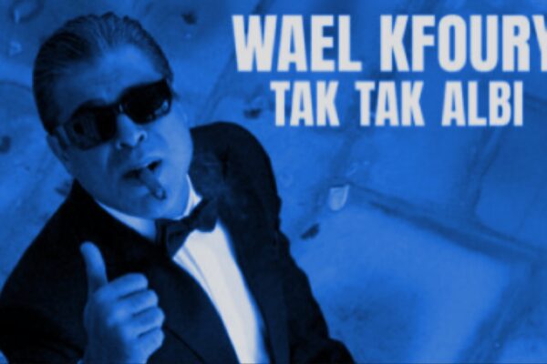 صورة وائل كفوري يرتدي بدلة رسمية وبنطلون أسود مع ربطة عنق بيضاء، يشير بإصبعه لأعلى ويضع نظارات شمسية، مع نص "وائل كفوري تك تك قلبي" في الخلفية الزرقاء.