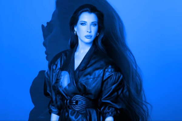 صورة لنانسي عجرم ترتدي جاكيتًا أسود بأسلوب عصري مع خلفية محدثة، تعكس أناقتها وجاذبيتها في الترويج لألبوم "نانسي 11"، مع ظلال فنية تضيف عمقًا للإطلالة.