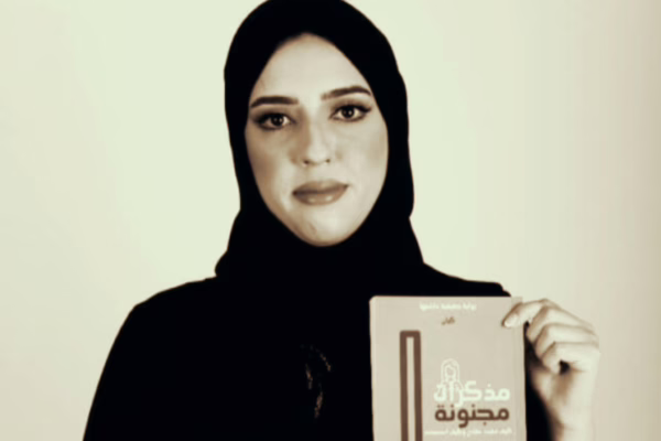 صورة لشيماء أحمد، كاتبة إماراتية ترتدي الحجاب الأسود، تحمل كتابها مذكرات مجنونة بلغة عربية، مع خلفية بيضاء فاتحة، تعبر عن قوتها وتجربتها الملهمة.