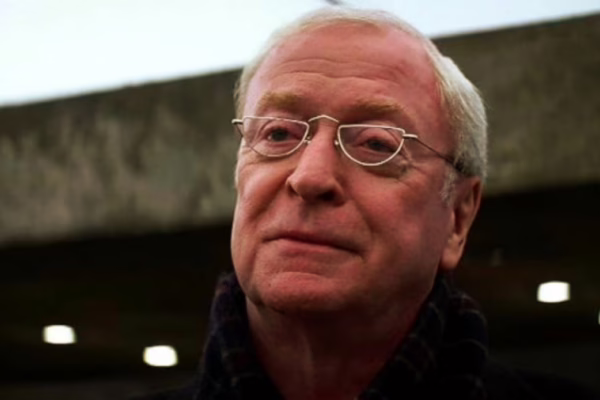 صورة مقربة للممثل الأسطوري السير مايكل كين في سن متقدم، يرتدي نظارة ويظهر عليه تعبير هادئ.