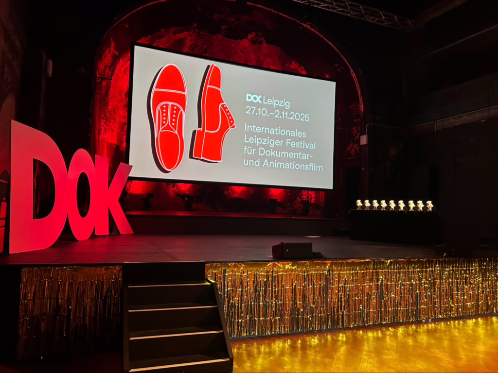 مسرح Schaubühne Lindenfels خلال حفل توزيع جوائز DOK Leipzig 2025، وتظهر جوائز الحمامة الذهبية على المسرح وشعار المهرجان وتواريخه على الشاشة الكبيرة.