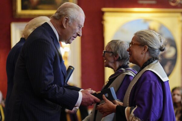 لقطة جانبية للملك تشارلز الثالث وهو يسلم جائزة لإحدى المكرمات التي ترتدي زياً أكاديمياً أرجوانياً في قصر سانت جيمز.