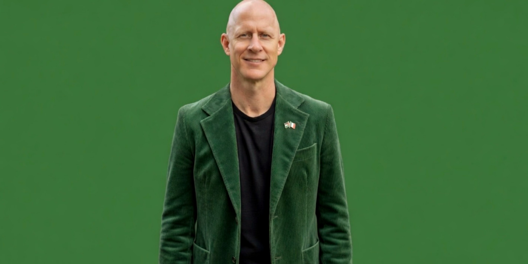 بورتريه رسمي لبرايان ماكغينيس (Brian McGinnis)، مرشح مجلس الشيوخ والمحارب القديم، يبتسم أمام خلفية خضراء، يرتدي سترة مخملية خضراء ودبوس العلم الفلسطيني على ياقته.