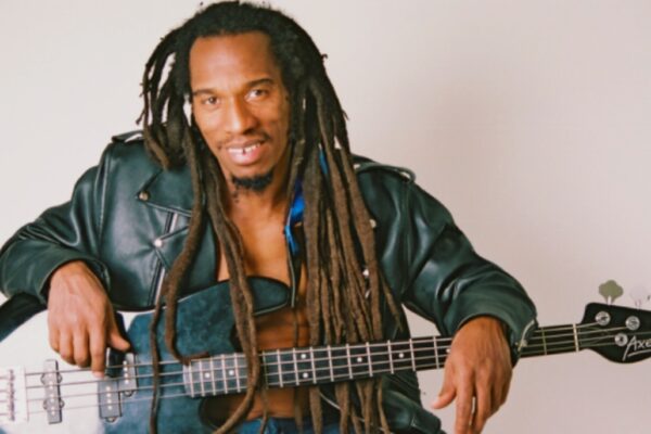 لقطة لبنيامين صفنيا، الشاعر والموسيقي البريطاني ذو شعر جديلة طويل (dreadlocks)، يجلس ويرتدي سترة جلدية سوداء، ممسكاً بغيتار باس أسود على خلفية بيضاء.