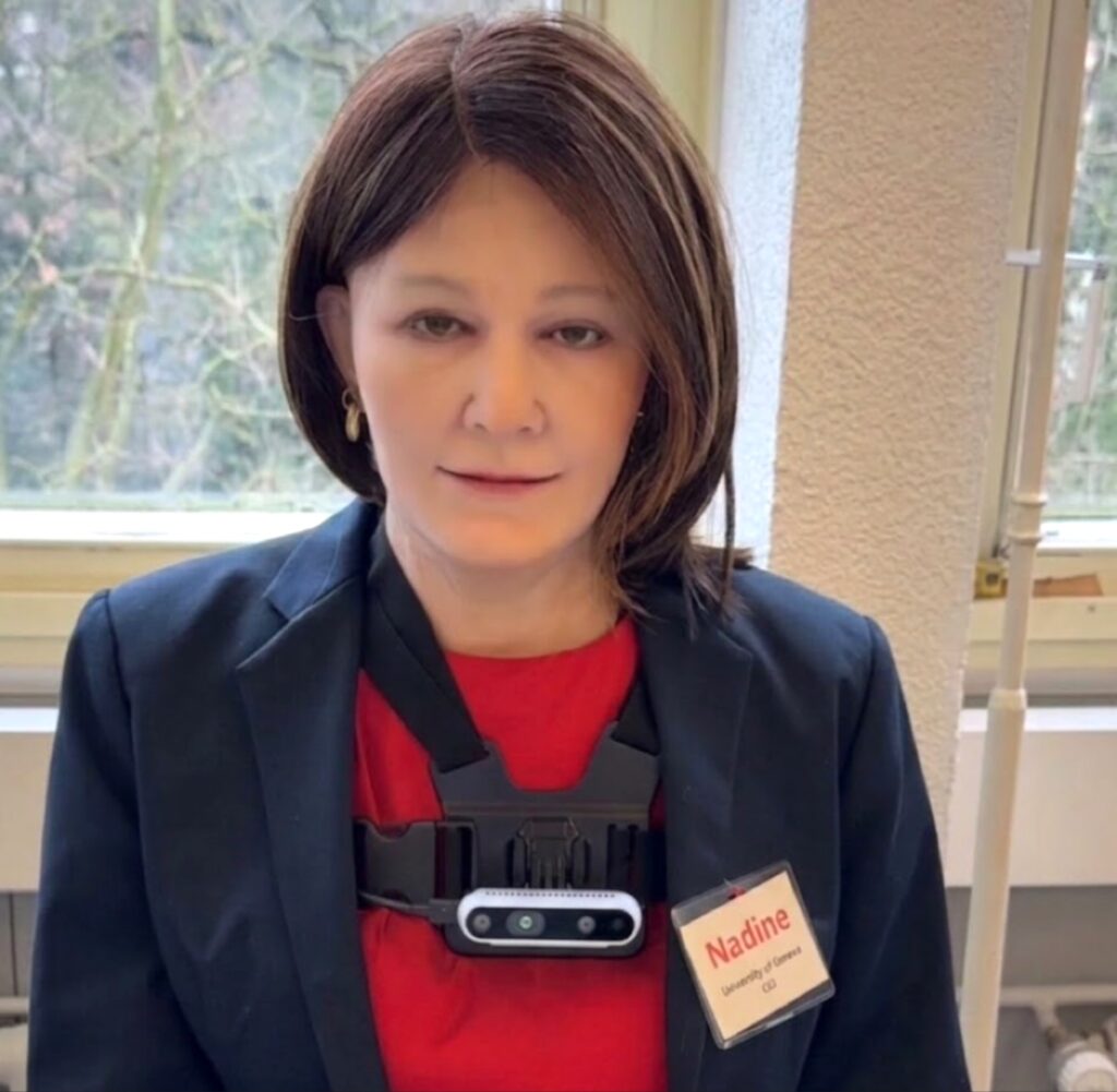 لقطة قريبة للروبوت الاجتماعي نادين (Nadine) بملامح بشرية واقعية ترتدي سترة سوداء وبطاقة تعريفية في معرض جنيف الدولي للاختراعات.