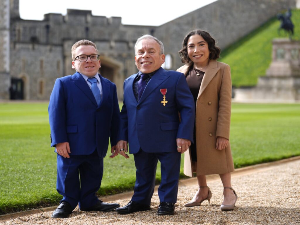 صورة تجمع الممثل وارويك ديفيس مع ابنته أنابيل وابنه هاريسون في ساحة قصر ويندسور، حيث يظهر ديفيس ببدلته الزرقاء ووسام OBE على صدره، في لقطة تذكارية عائلية عقب مراسم التكريم الملكي.