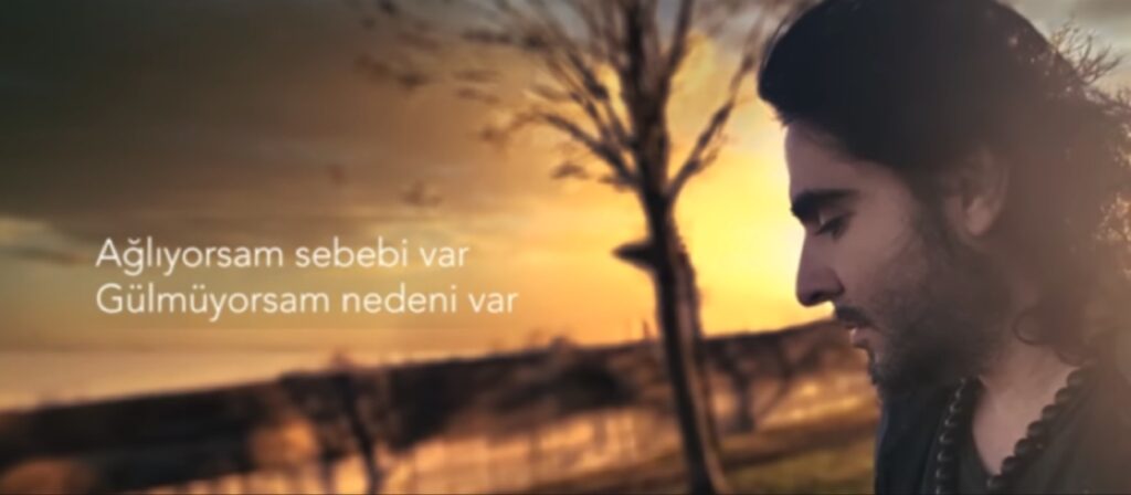 لقطة جانبية (بروفايل) تظهر ملامح وجه تنظر إلى الأسفل بتعبير حزين، مقابل خلفية ضبابية درامية لغروب الشمس الذهبي والبرتقالي، مع بروز شجيرة جافة داكنة ونص تركي باللون الأبيض يظهر بوضوح على الجانب الأيسر.