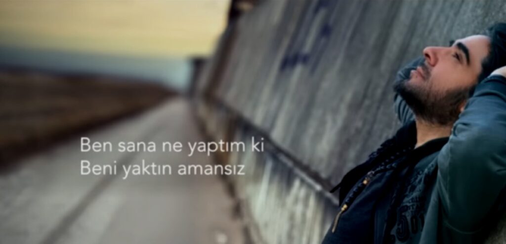 كادر سينمائي يظهر ملامح وجه يرتدي سترة خضراء بنظرات شاردة، وتظهر بجانبه ترجمة نصية لأبيات شعرية باللغة التركية تصف مشاعر الحزن واليأس التي يتركها الفراق في الوجدان.