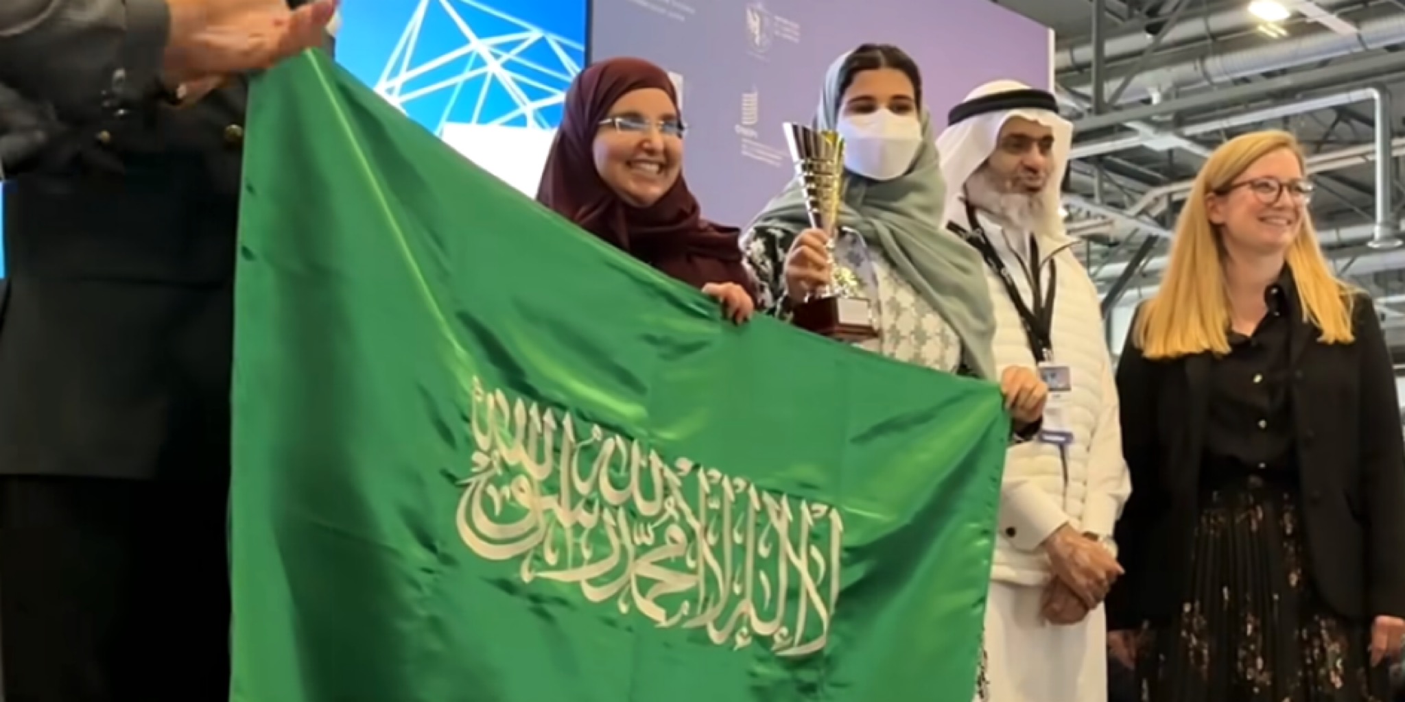 الجوهرة القحطاني ترفع العلم السعودي وتحمل كأس الجائزة الكبرى في معرض جنيف الدولي للاختراعات 2026.