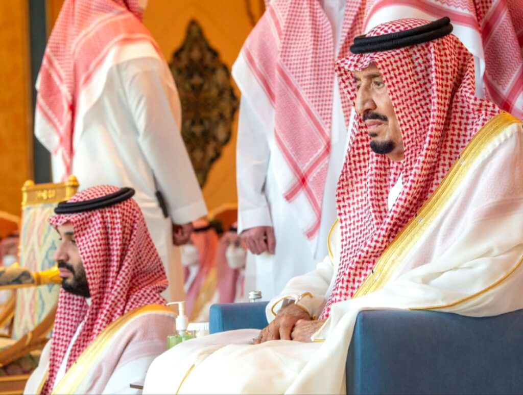 صورة رسمية تجمع خادم الحرمين الشريفين الملك سلمان بن عبد العزيز وولي العهد الأمير محمد بن سلمان، وهما جالسان في مجلس فخم، يرتديان البشوت السعودية التقليدية.