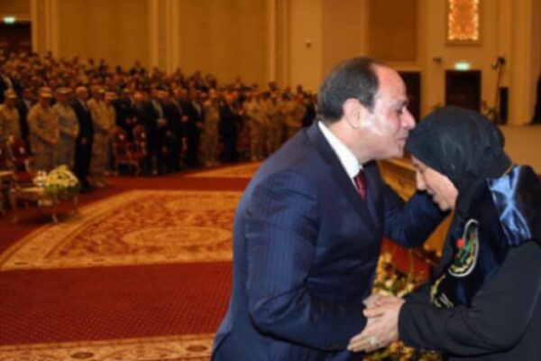 لقطة مؤثرة تجسد البرّ والتقدير، تظهر فخامة الرئيس عبد الفتاح السيسي وهو يقبل رأس سيدة مسنة (أم مصرية مكافحة) ويصافحها على خشبة المسرح خلال احتفالية رسمية بـ عيد الأم، في قاعة كبرى بحضور كثيف من الشخصيات الرسمية والعسكرية.