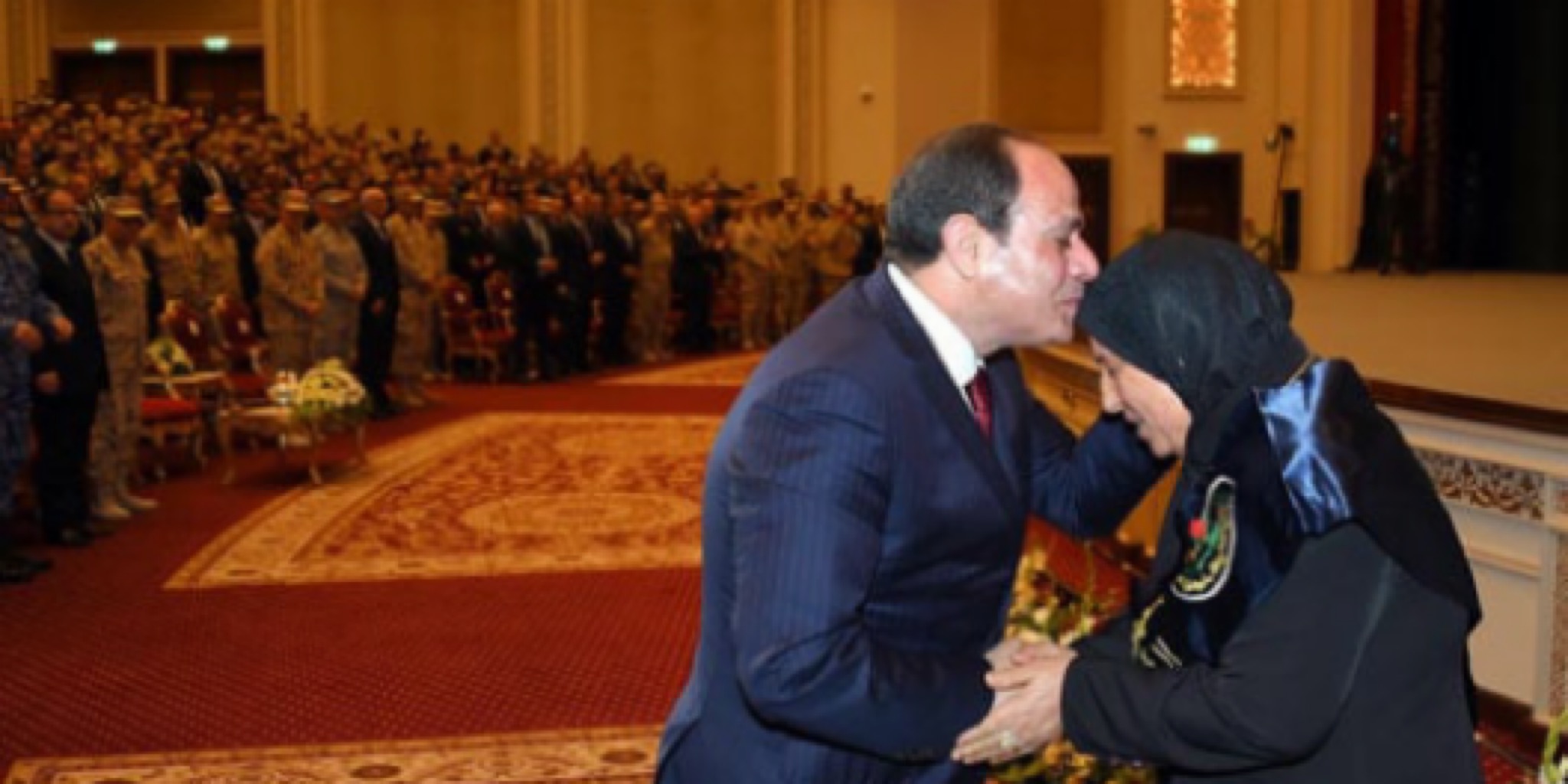 لقطة مؤثرة تجسد البرّ والتقدير، تظهر فخامة الرئيس عبد الفتاح السيسي وهو يقبل رأس سيدة مسنة (أم مصرية مكافحة) ويصافحها على خشبة المسرح خلال احتفالية رسمية بـ عيد الأم، في قاعة كبرى بحضور كثيف من الشخصيات الرسمية والعسكرية.