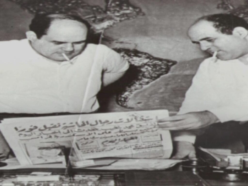 صورة تاريخية بالأبيض والأسود تجمع بين الكاتبين علي ومصطفى أمين وهما يدخنان ويطالعان صحيفة "أخبار اليوم" في مكتبهما، وتظهر خلفهما خريطة عالمية معلقة على الجدار.