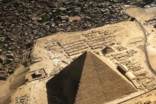 لقطة جوية من نافذة طائرة تظهر هرم خوفو الأكبر ومنطقة الأهرامات في الجيزة مع الكتلة السكنية المحيطة بالقاهرة تحت أشعة الشمس.