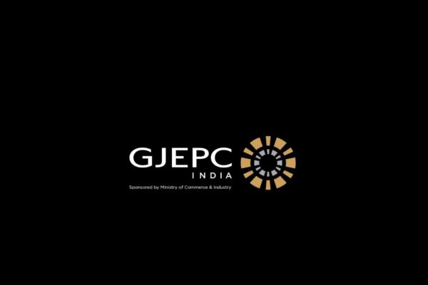 شعار مجلس تعزيز تصدير الأحجار الكريمة والمجوهرات (GJEPC INDIA) باللون الأبيض، ترافقه أيقونة دائرية هندسية باللونين الذهبي والرمادي ترمز للقطاع، مع نص في الأسفل يشير إلى رعاية وزارة التجارة والصناعة الهندية، الكل يظهر بوضوح على خلفية سوداء صماء.