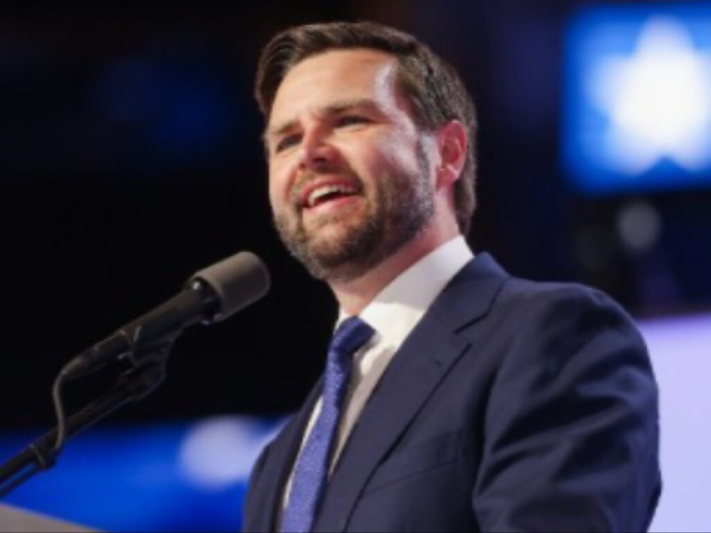 نائب الرئيس الأمريكي جيه دي فانس يتحدث خلف المنصة وهو يبتسم بثقة أثناء خطاب عام.