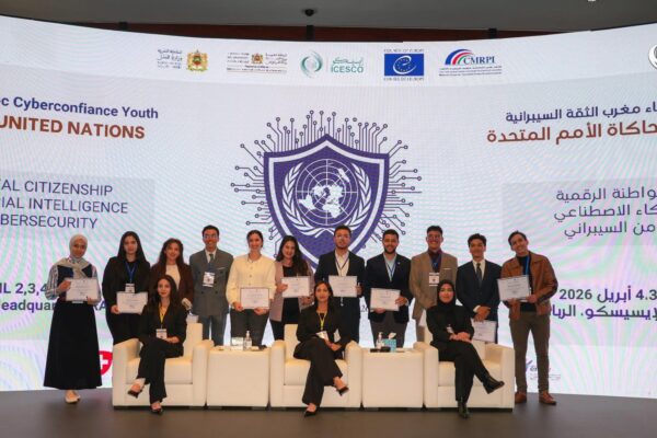 صورة جماعية لشباب وشابات يقفون على منصة في مقر الإيسيسكو بالرباط، يحملون شهادات تقديرية أمام شاشة رقمية ضخمة تظهر شعار المنظمة وعبارة "نموذج محاكاة الأمم المتحدة" باللغتين العربية والإنجليزية، مع محاور الفعالية: المواطنة الرقمية، الذكاء الاصطناعي، والأمن السيبراني، ضمن حدث محاكاة الأمم المتحدة للإيسيسكو المقام في أبريل 2026.