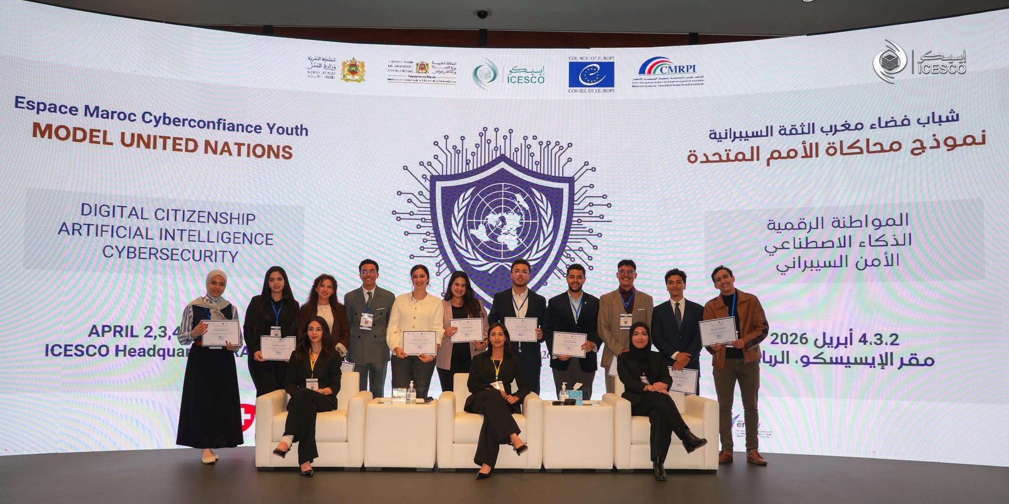 صورة جماعية لشباب وشابات يقفون على منصة في مقر الإيسيسكو بالرباط، يحملون شهادات تقديرية أمام شاشة رقمية ضخمة تظهر شعار المنظمة وعبارة "نموذج محاكاة الأمم المتحدة" باللغتين العربية والإنجليزية، مع محاور الفعالية: المواطنة الرقمية، الذكاء الاصطناعي، والأمن السيبراني، ضمن حدث محاكاة الأمم المتحدة للإيسيسكو المقام في أبريل 2026.
