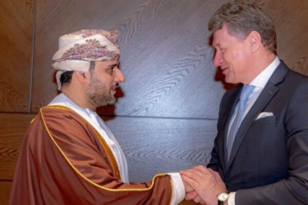 تصافح رسمي بين الشيخ فيصل بن عبدالله الرواس رئيس غرفة تجارة وصناعة عُمان ومكسيم فلاديميروفيتش ريزينكوف وزير خارجية بيلاروس، في قاعة ختام منتدى الأعمال العُماني البيلاروسي لعام 2026، يرتدي الرواس البشت التقليدي وريزينكوف البدلة والرباط، على خلفية لوح خشبي.