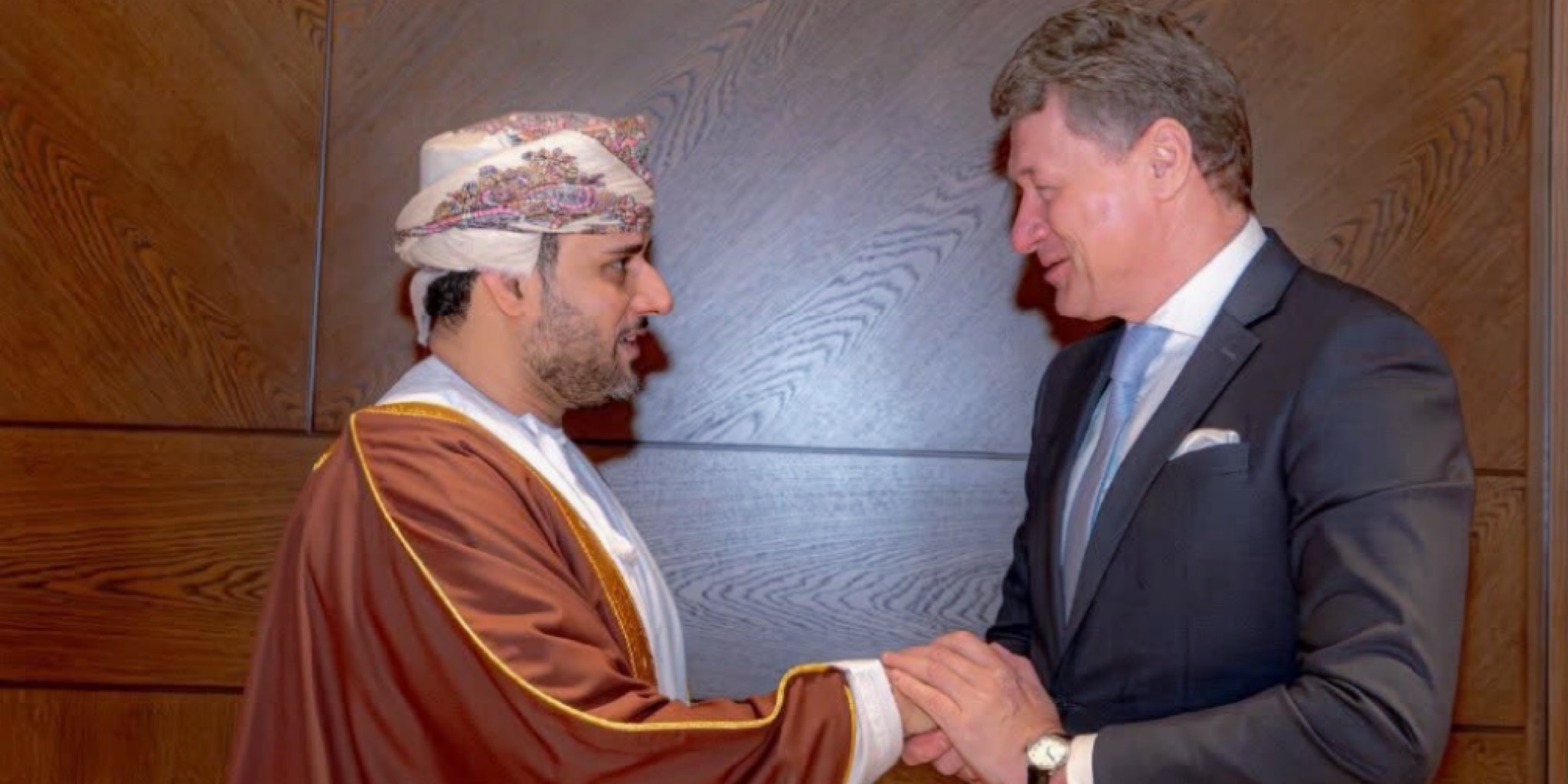 تصافح رسمي بين الشيخ فيصل بن عبدالله الرواس رئيس غرفة تجارة وصناعة عُمان ومكسيم فلاديميروفيتش ريزينكوف وزير خارجية بيلاروس، في قاعة ختام منتدى الأعمال العُماني البيلاروسي لعام 2026، يرتدي الرواس البشت التقليدي وريزينكوف البدلة والرباط، على خلفية لوح خشبي.