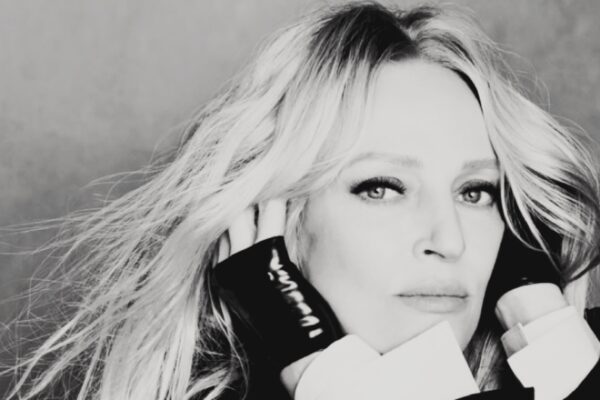 صورة بالأبيض والأسود قريبة لوجه النجمة أوما ثورمان، تنظر للكاميرا بنظرة ثاقبة وشعر يتطاير، وهي ترتدي قفازات سوداء لامعة، في لقطة رسمية.