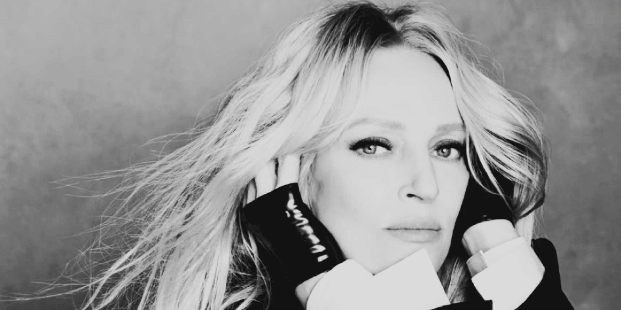 صورة بالأبيض والأسود قريبة لوجه النجمة أوما ثورمان، تنظر للكاميرا بنظرة ثاقبة وشعر يتطاير، وهي ترتدي قفازات سوداء لامعة، في لقطة رسمية.