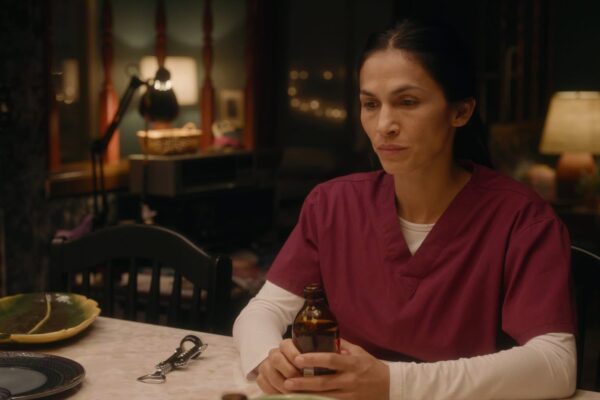 Élodie Yung تجلس بملامح حزينة ممسكة بزجاجة دواء في مشهد درامي من مسلسل The Cleaning Lady.