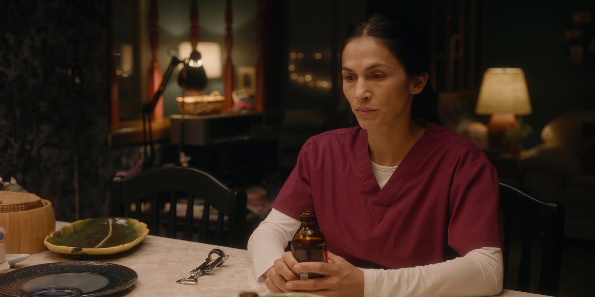 Élodie Yung تجلس بملامح حزينة ممسكة بزجاجة دواء في مشهد درامي من مسلسل The Cleaning Lady.