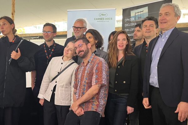 صورة تذكارية لأعضاء تحالف المهرجانات السينمائية الأوروبية (Doc Alliance)، تظهر امرأة تتحدث في ميكروفون ولافتات "DOK Leipzig" و"Marché du Film" خلفهم، خلال حفل مرتبط بـ جائزة Doc Alliance Award 2026.