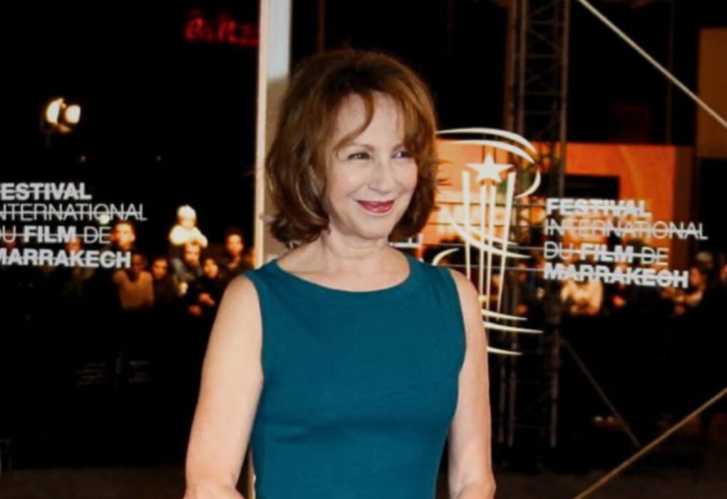 لقطة متوسطة للممثلة ناتالي باي بفستان أزرق داكن، تبتسم وتنظر إلى اليسار، مع ظهور واضح لشعار "FESTIVAL INTERNATIONAL DU FILM DE MARRAKECH" على خلفية مضيئة خلفها.