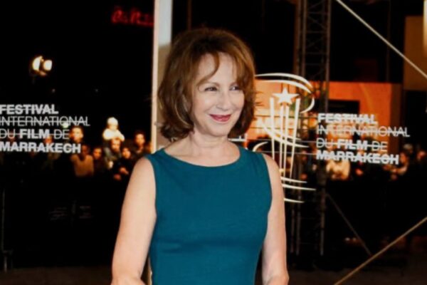 لقطة متوسطة للممثلة ناتالي باي بفستان أزرق داكن، تبتسم وتنظر إلى اليسار، مع ظهور واضح لشعار "FESTIVAL INTERNATIONAL DU FILM DE MARRAKECH" على خلفية مضيئة خلفها.