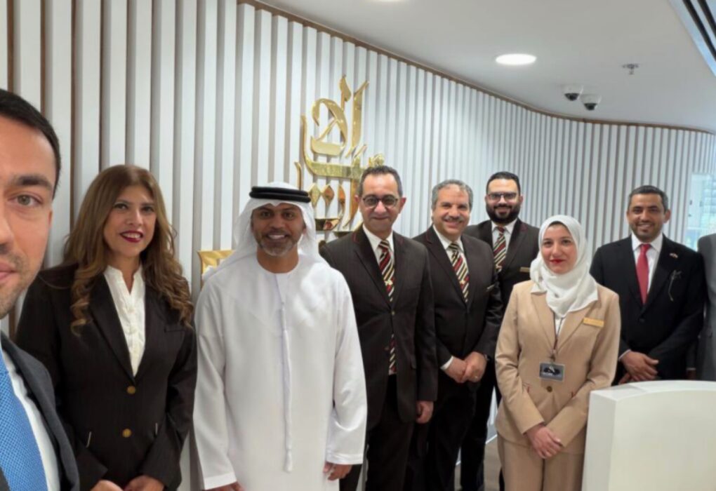 صورة سيلفي تظهر السفير الإماراتي حمد عبيد الزعابي محاطاً بموظفي مكتب طيران الإمارات في مصر الذين يرتدون الزي الرسمي، ويظهر خلفهم شعار الشركة على جدار خشبي مزخرف في بيئة مكتبية عصرية لعام 2026.