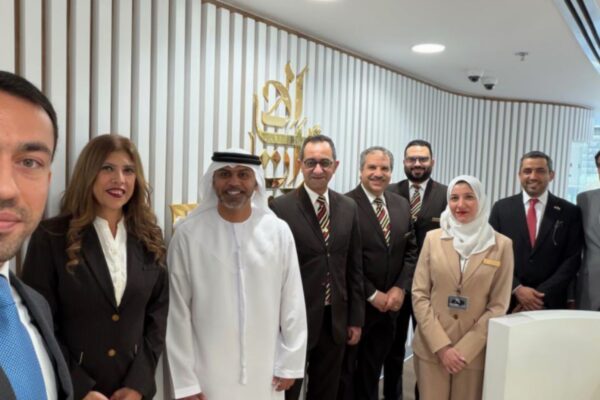 صورة سيلفي تظهر السفير الإماراتي حمد عبيد الزعابي محاطاً بموظفي مكتب طيران الإمارات في مصر الذين يرتدون الزي الرسمي، ويظهر خلفهم شعار الشركة على جدار خشبي مزخرف في بيئة مكتبية عصرية لعام 2026.