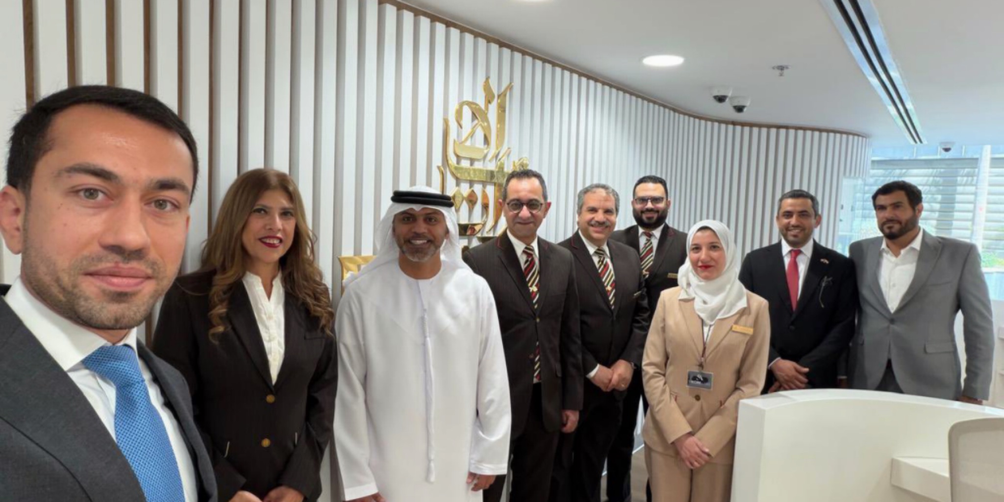صورة سيلفي تظهر السفير الإماراتي حمد عبيد الزعابي محاطاً بموظفي مكتب طيران الإمارات في مصر الذين يرتدون الزي الرسمي، ويظهر خلفهم شعار الشركة على جدار خشبي مزخرف في بيئة مكتبية عصرية لعام 2026.