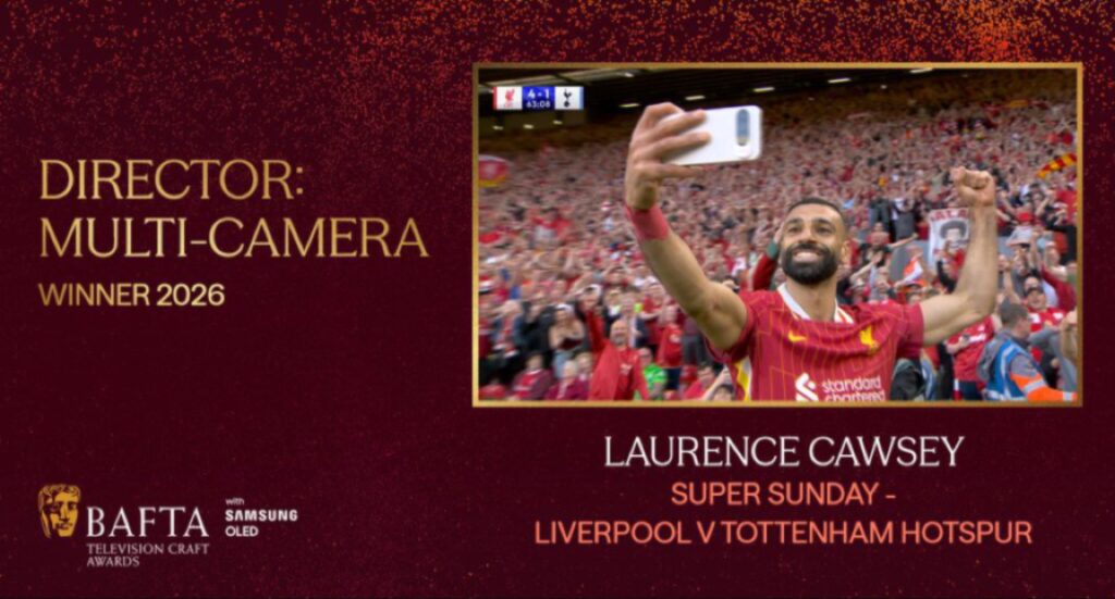 رسم غرافيكي رسمي ضمن جوائز بافتا كرافت يعلن فوز لورانس كاوسي بجائزة 'مخرج: كاميرا متعددة' لعام 2026 عن تغطية مباراة 'الأحد الممتاز - ليفربول ضد توتنهام هوتسبير'. الصورة المركزية تظهر لاعب ليفربول محمد صلاح وهو يرفع هاتفه لالتقاط صورة سيلفي محتفلًا مع الجمهور المبتهج في المدرجات خلفه، مع لوحة نتائج صغيرة تظهر نتيجة LIV 4-3 TOT. يتضمن الغرافيك شعارات بافتا وسامسونج OLED.