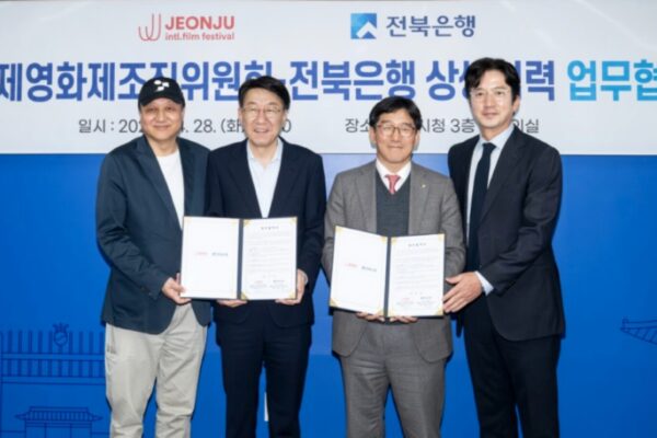 أربعة مسؤولين، من بينهم وو بيوم غي وبارك تشون وون، يبتسمون ويحملون نسخاً مفتوحة من الاتفاقية خلال مَراسم توقيع شراكة مهرجان جونجو المصرفية بمركز بلدية جونجو، مع لافتة خلفية باللغة الكورية تحمل شعارات المهرجان وبنك جيونبوك.