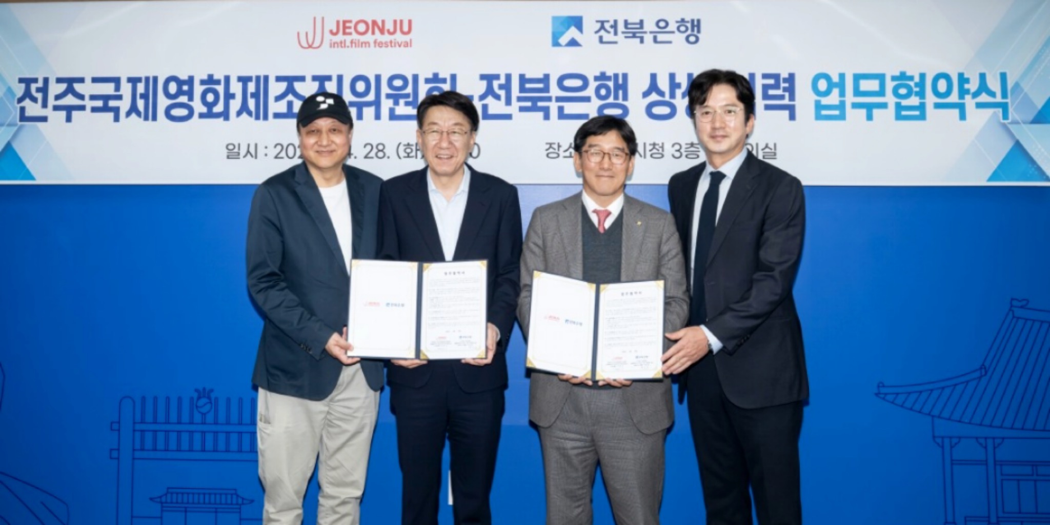 أربعة مسؤولين، من بينهم وو بيوم غي وبارك تشون وون، يبتسمون ويحملون نسخاً مفتوحة من الاتفاقية خلال مَراسم توقيع شراكة مهرجان جونجو المصرفية بمركز بلدية جونجو، مع لافتة خلفية باللغة الكورية تحمل شعارات المهرجان وبنك جيونبوك.