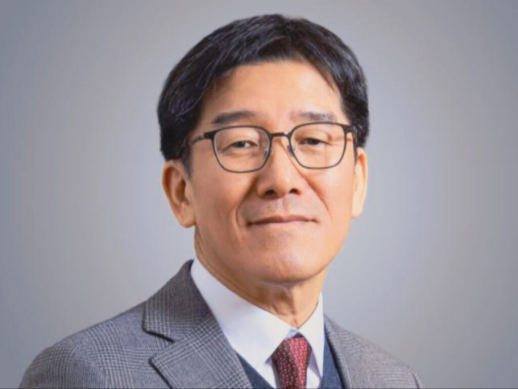 صورة رسمية لرئيس بنك جيونبوك (بارك تشون وون)، يرتدي نظارة وسترة بدلة رمادية منقوشة وربطة عنق، يبتسم بثقة وينظر إلى الكاميرا على خلفية رمادية بسيطة.