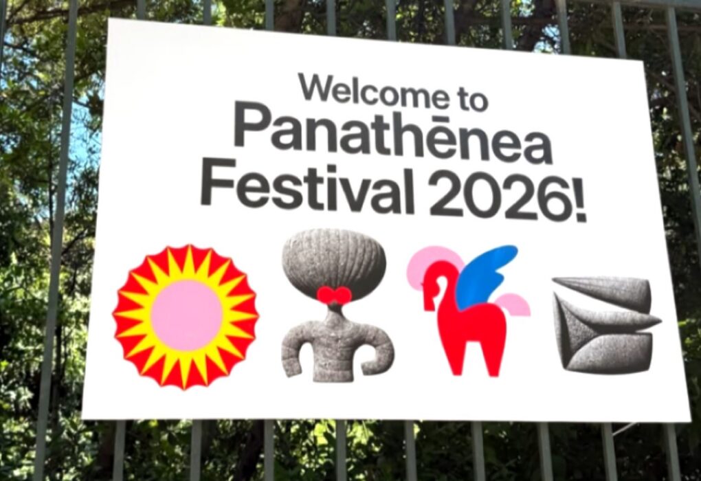 شعار مهرجان باناثينيا 2026 الترحيبي على لافتة بيضاء معلقة وسط الأشجار، يتضمن عبارة Welcome to Panathēnea Festival 2026 والرموز البصرية المميزة للمهرجان
