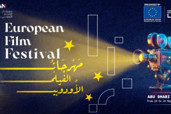 ملصق دعائي لمهرجان الفيلم الأوروبي - الإمارات 2026. يظهر على اليسار مبنى تاريخي إماراتي مضاء ونخلة واحدة. في الوسط، تحت شعاع ضوئي أصفر قادم من كاميرا سينمائية عتيقة على اليمين، يظهر نص كبير باللغتين الإنجليزية والعربية: "European Film Festival" و "مهرجان الفيلم الأوروبي". الخلفية زرقاء داكنة مع نجوم ورموز خطية بيضاء.
