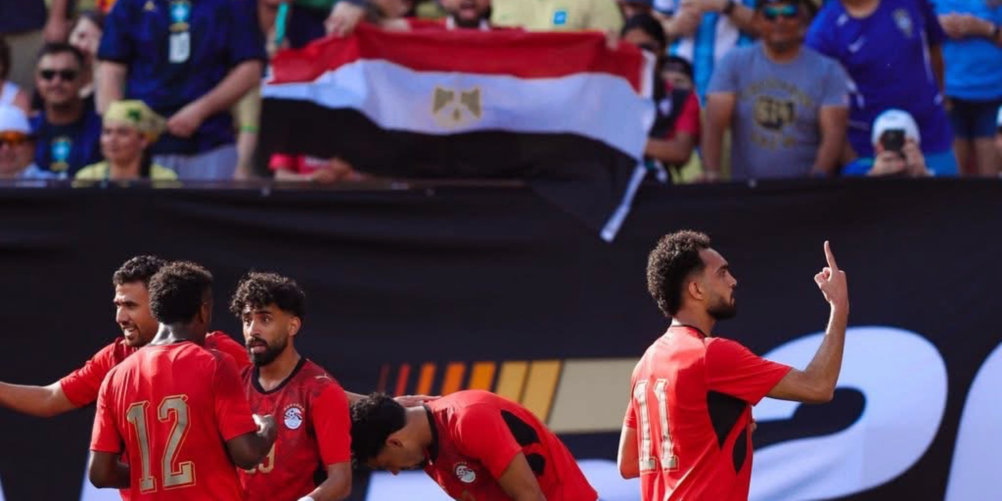 لاعبو منتخب مصر يحتفلون أمام الجماهير التي ترفع العلم المصري في المدرجات خلال أحداث مباراة مصر والبرازيل التحضيرية واحتفالا بهدف اللاعب مصطفى زيكو