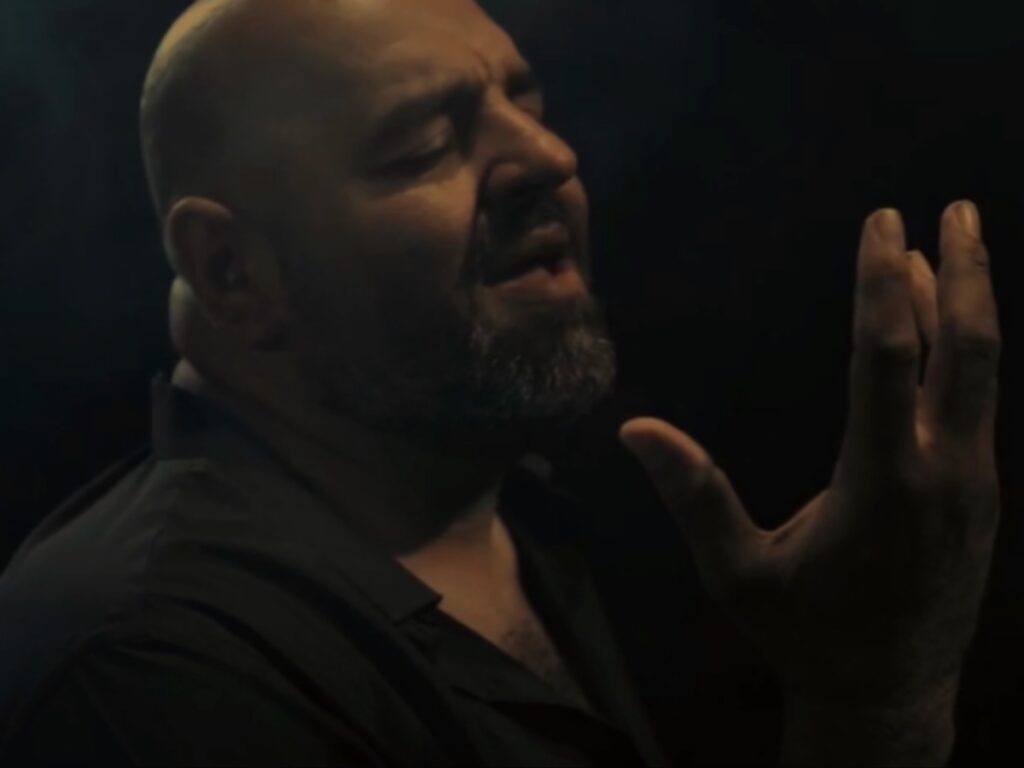 لقطة مقربة تبرز تأثر واندماج المطرب أحمد الحلواني رافعاً يده أثناء الغناء في الظلام ضمن إصدار جديد