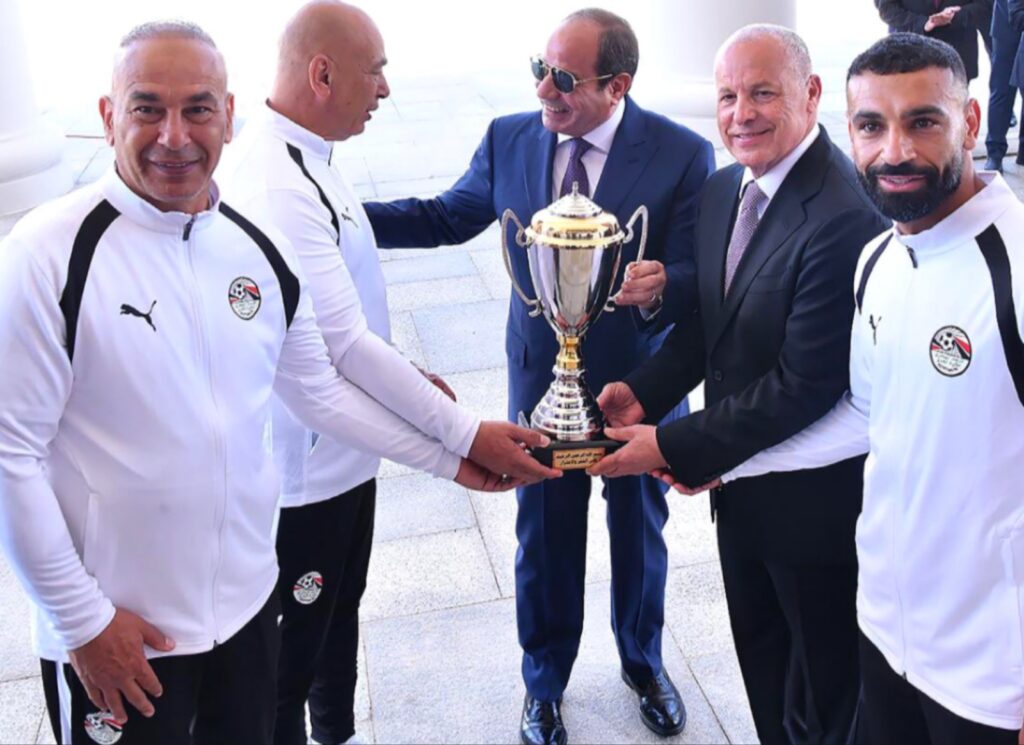 فخامة الرئيس عبد الفتاح السيسي يبتسم أثناء حمله كأس الجدارة بمشاركة التوأم حسام وإبراهيم حسن وبعض الحضور على هامش تكريم المنتخب الوطني المصري