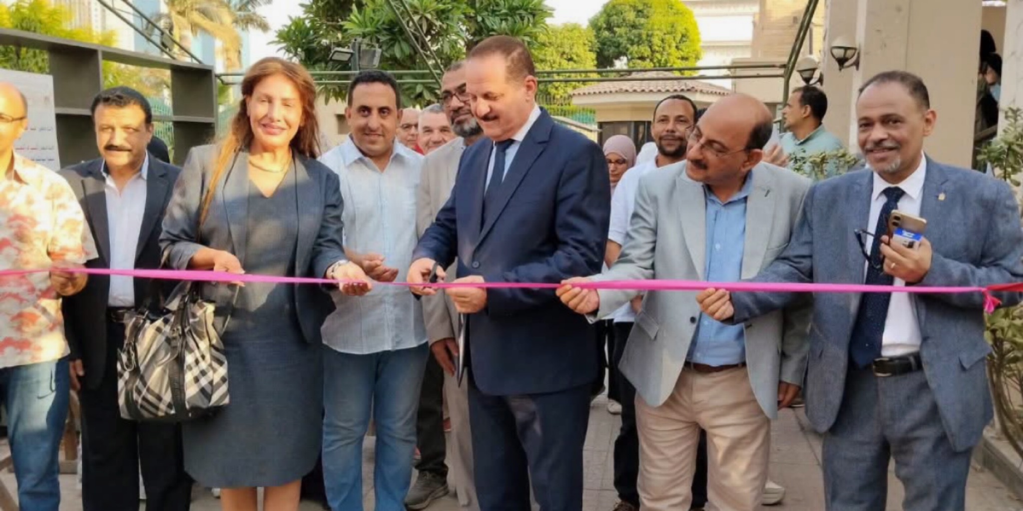 قيادات ثقافية ومسؤولون يقومون بقص شريط الافتتاح لمعرض فني في ساحة خارجية، وسط حضور عدد من المشاركين والمهتمين
