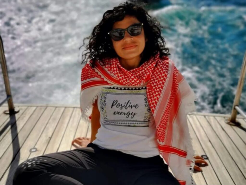 صانعة الأفلام الرومانية ترتدي وشاحاً أحمر وقميصاً يحمل عبارة طاقة إيجابية أثناء جلوسها على قارب