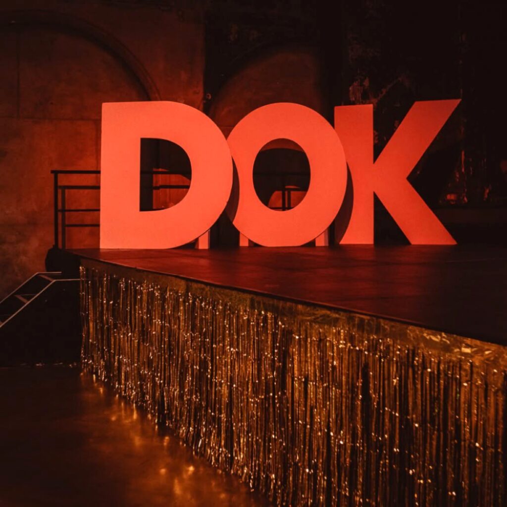 مجسم ضخم باللون الأحمر لحروف DOK يزين منصة مسرح ذات إضاءة خافتة استعداداً لانطلاق فعاليات معرض DOK Neuland التفاعلي